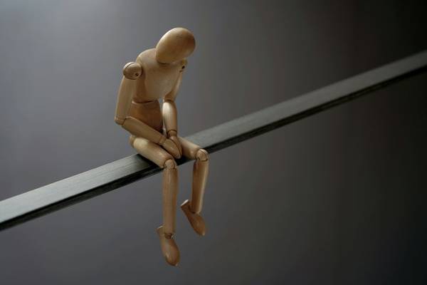 Holzfigur sitzt mit gesenktem Kopf und verschränkten Händen auf einer Kante